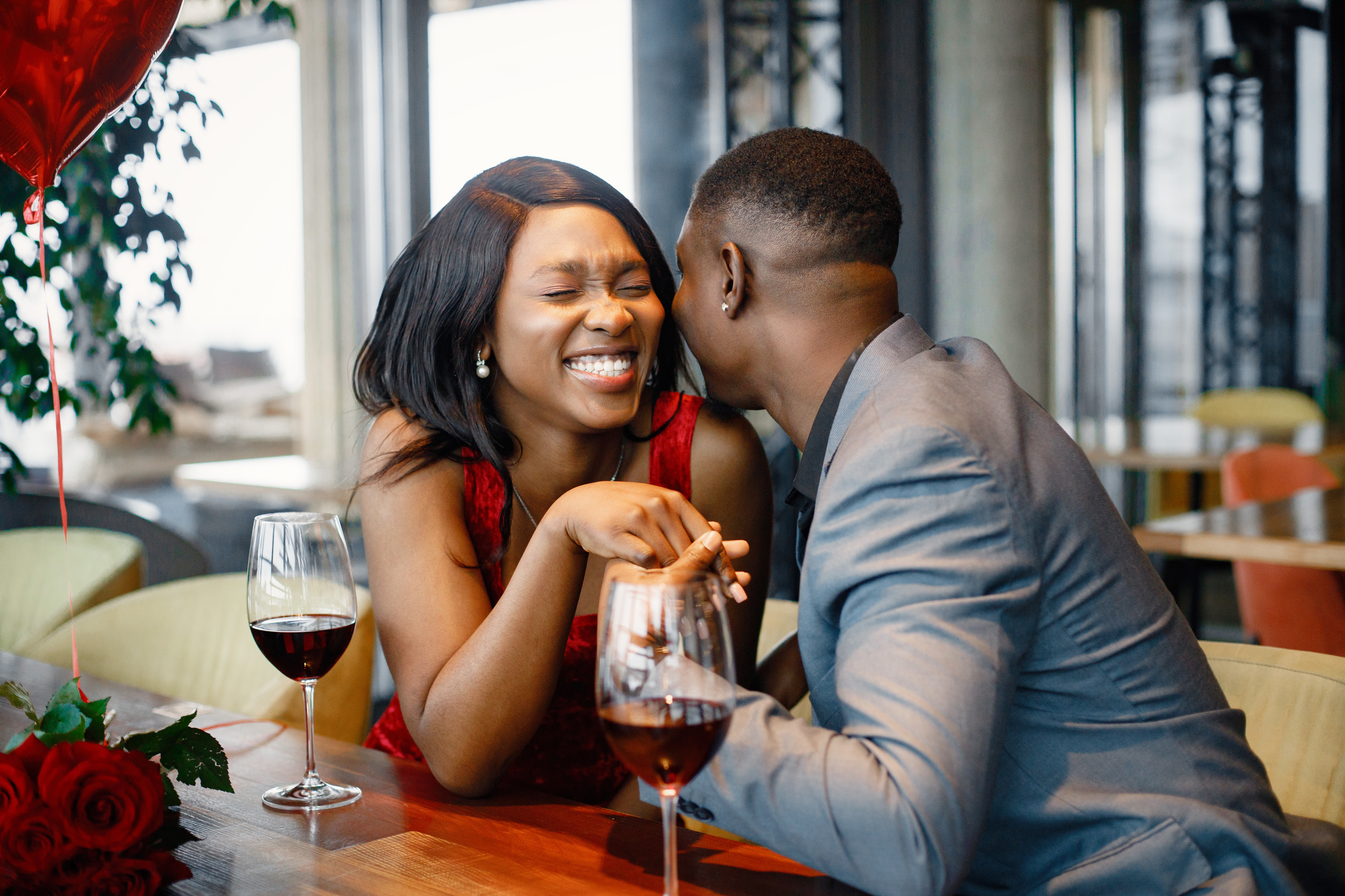 Couple enjoying day out at restaurant. Black man and woman talking and holding hands. Woman wearing red elegant dress and man blue costume.
